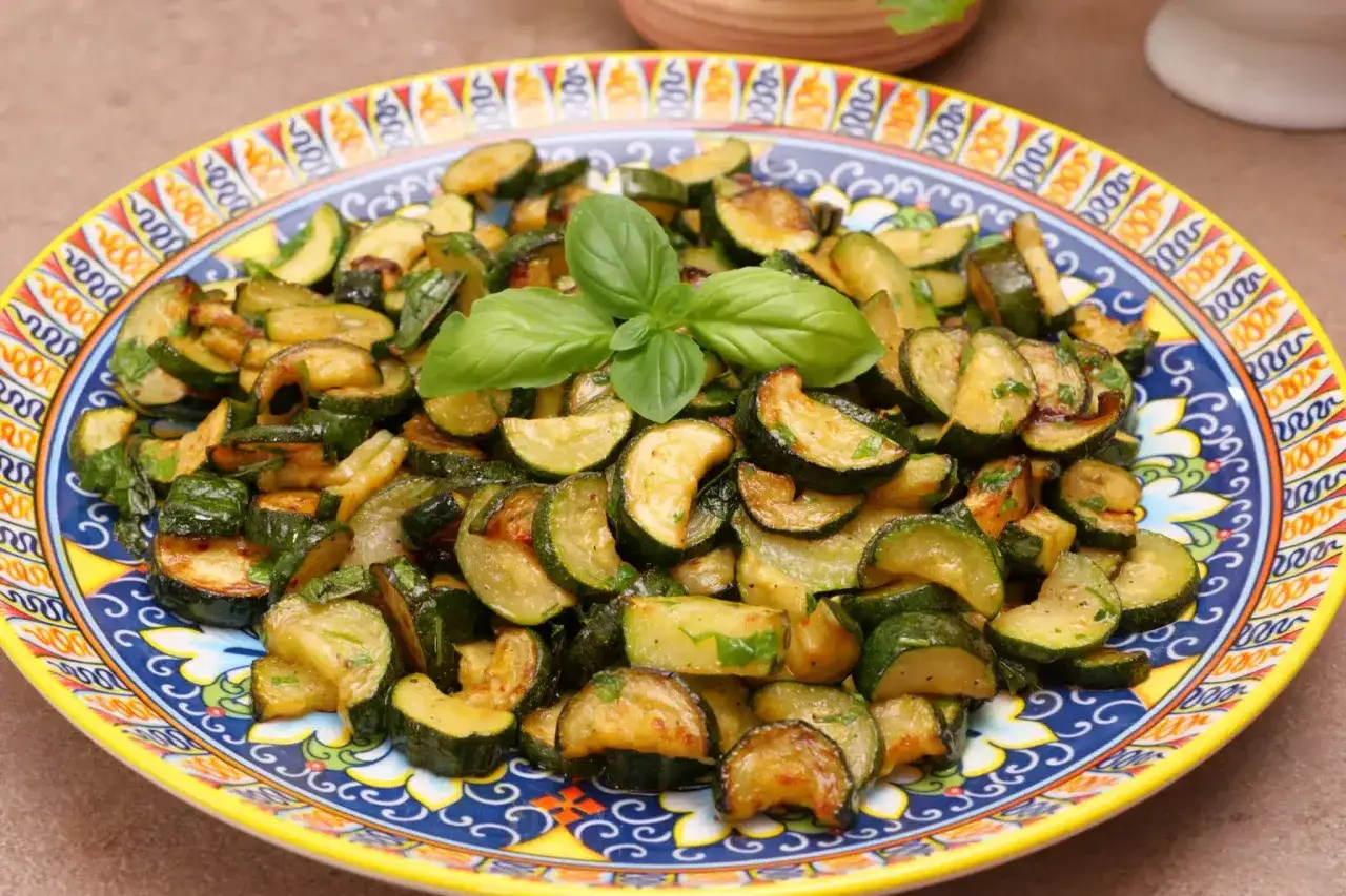 Zucchine in padella, dorate e saporite, guarnite con basilico fresco su un piatto decorato.