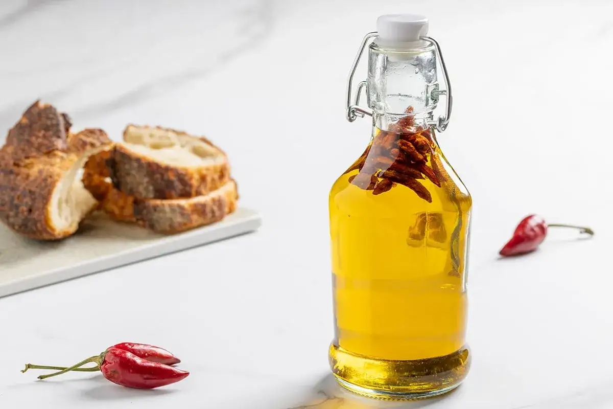 Bottiglia di olio al peperoncino con peperoncini rossi e fette di pane rustico.