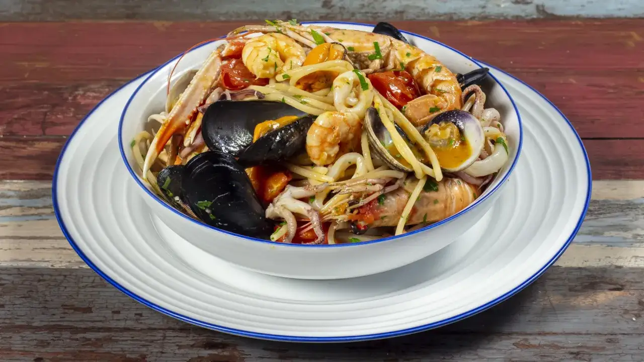 Un invitante piatto di spaghetti allo scoglio, ricco di gamberi, cozze, vongole e calamari, condito con pomodorini e prezzemolo.