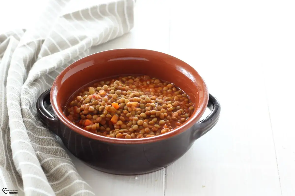 Un piatto fumante di lenticchie in umido, con carote e pomodoro, servito in una ciotola di terracotta.