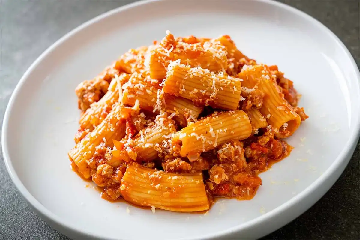 Piatto di pasta alla zozzona, con rigatoni conditi con un ricco rag&ugrave; di carne e pomodoro, spolverati di parmigiano.