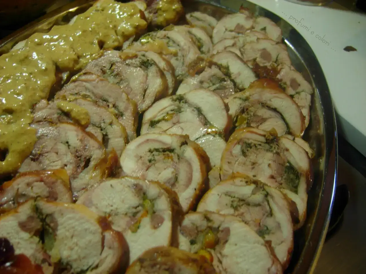 Fette di coniglio al forno, farcito e succulento, servito su un vassoio con una salsa dorata.