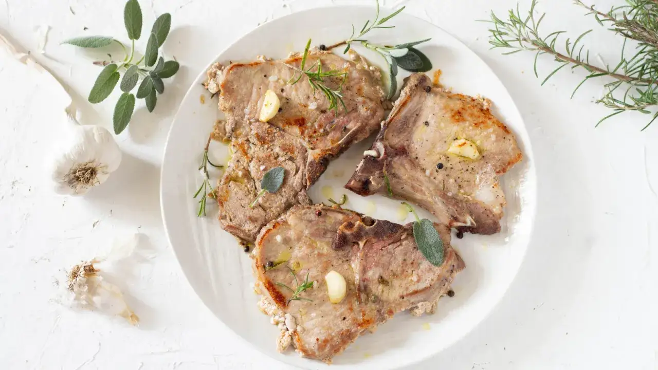 Tre succulente braciole di maiale cotte alla perfezione, guarnite con aglio, rosmarino e salvia.