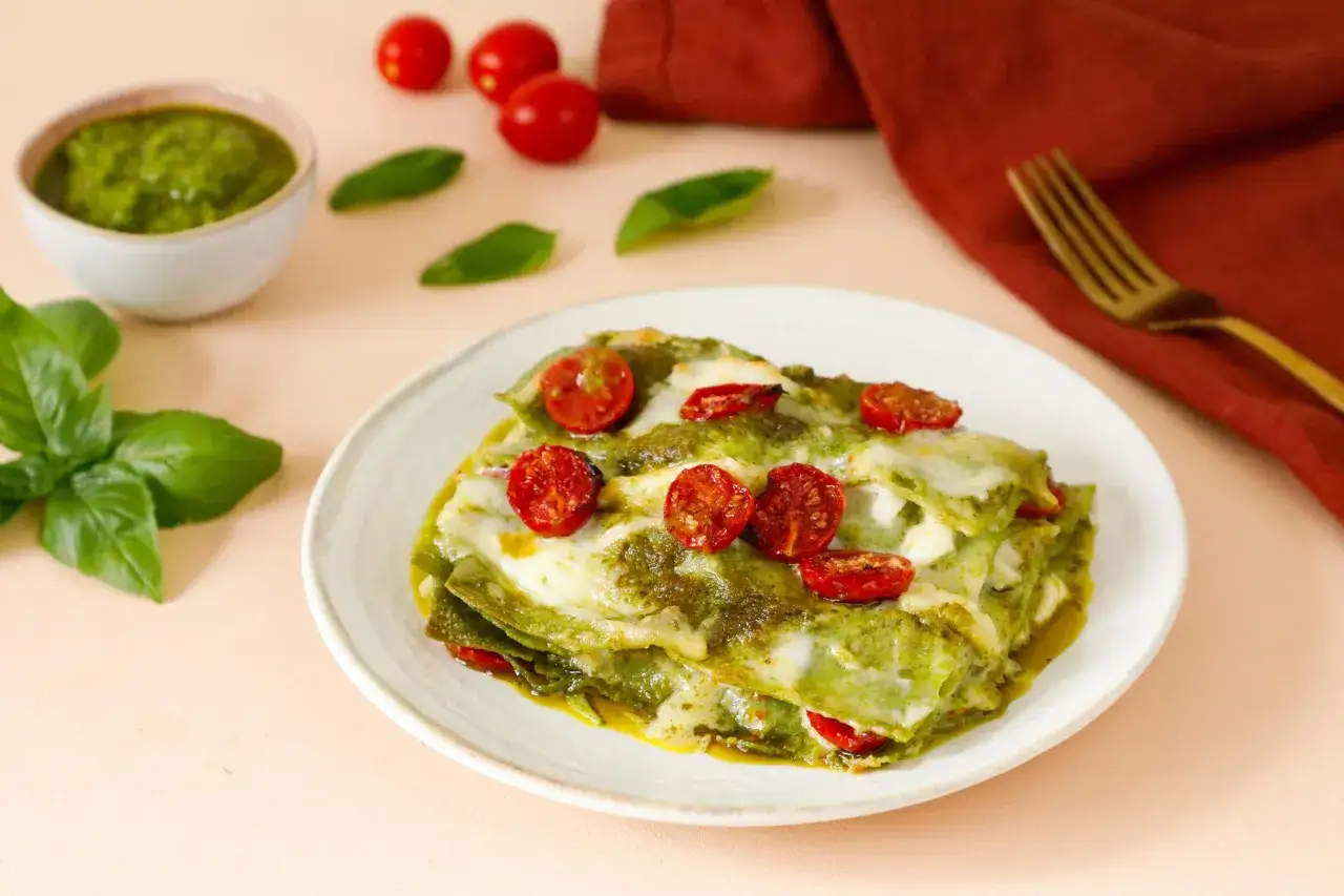 Un piatto di lasagne al pesto, con pomodorini e mozzarella filante, pronto per essere gustato.