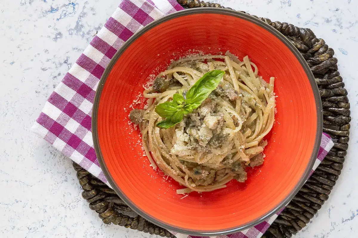 Un piatto invitante di pasta con melanzane e pancetta, guarnito con basilico fresco e parmigiano.