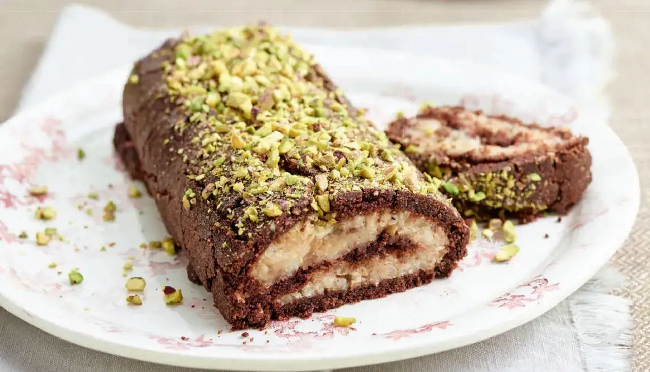 Rotolo al cioccolato e pistacchio, un dolce con farina di riso, ripieno di crema chiara e cacao, cosparso di granella verde.