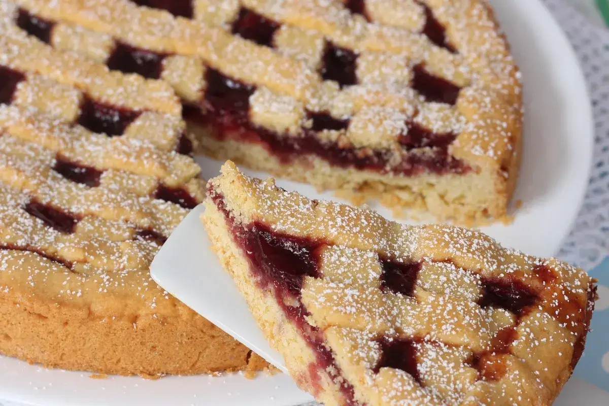 Deliziosa crostata senza burro con marmellata di ciliegie, cosparsa di zucchero a velo. Una fetta è già servita.