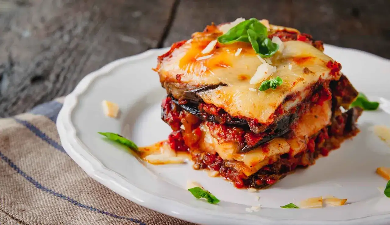 Una fetta di parmigiana di melanzane, ricca e gustosa, con strati di melanzane, sugo e formaggio filante, guarnita con basilico fresco.