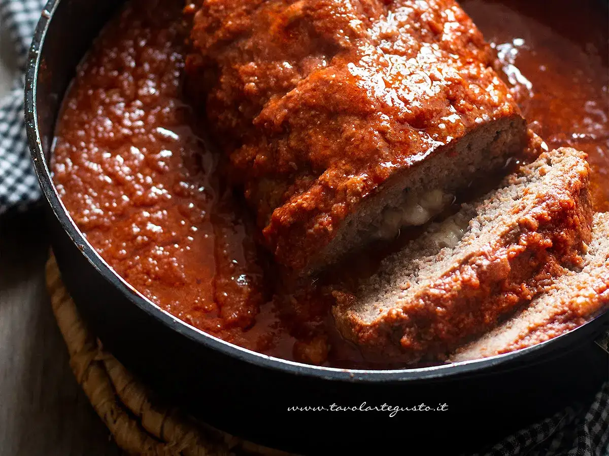 Un succulento polpettone al forno, affogato in un ricco sugo di pomodoro, con una fetta tagliata che rivela un cuore filante di formaggio.