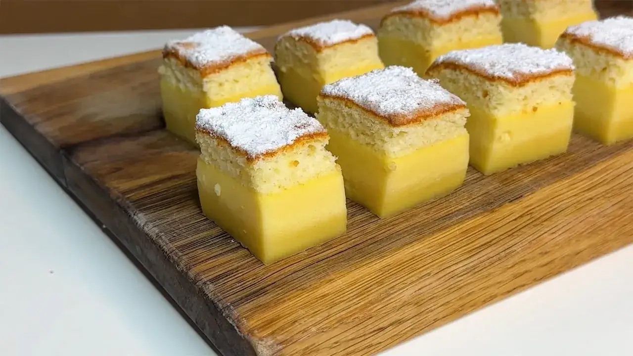 Porzioni di torta magica ricetta, con base soffice e crema gialla, spolverate di zucchero a velo, su tagliere di legno.