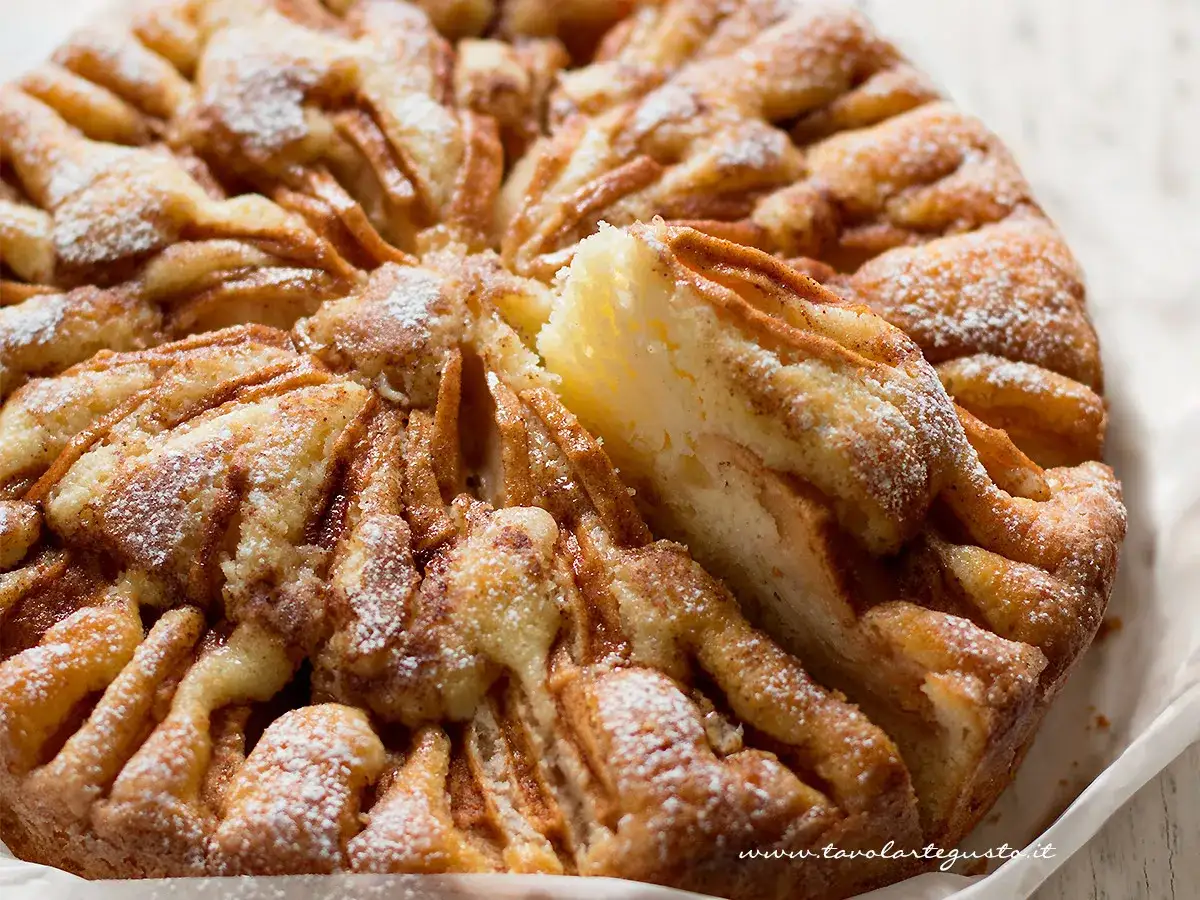Una deliziosa torta di mele, cosparsa di zucchero a velo, con una fetta rimossa che mostra la morbida consistenza.