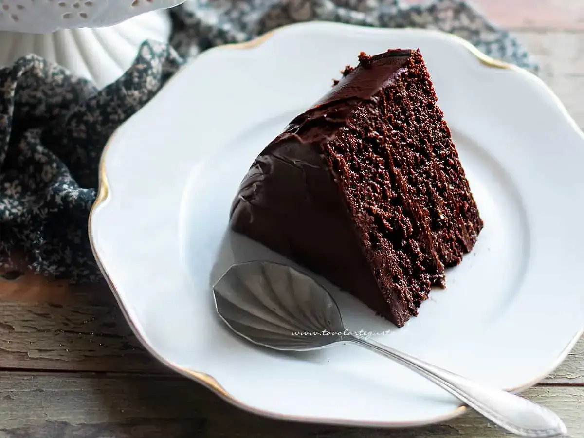 Una fetta di torta al cioccolato, umida e golosa, su un piatto bianco con un cucchiaino d'argento.