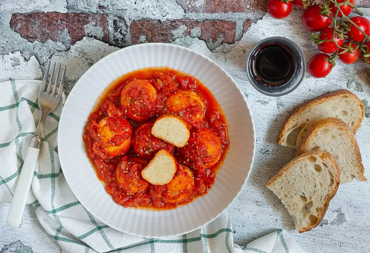 Deliziose polpette di ricotta in salsa di pomodoro, servite con pane casereccio e un bicchiere di vino rosso.