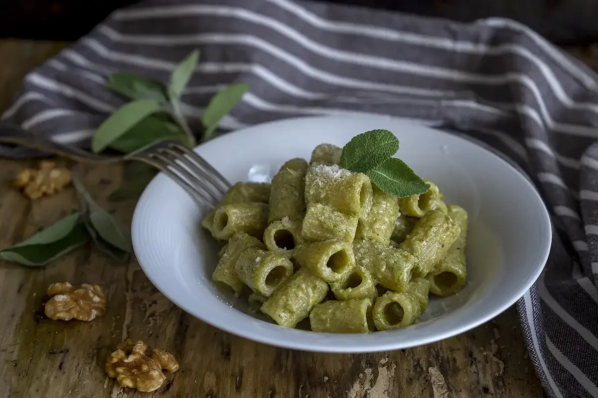 Piatto di rigatoni conditi con un saporito pesto di salvia e noci, guarnito con foglie fresche.