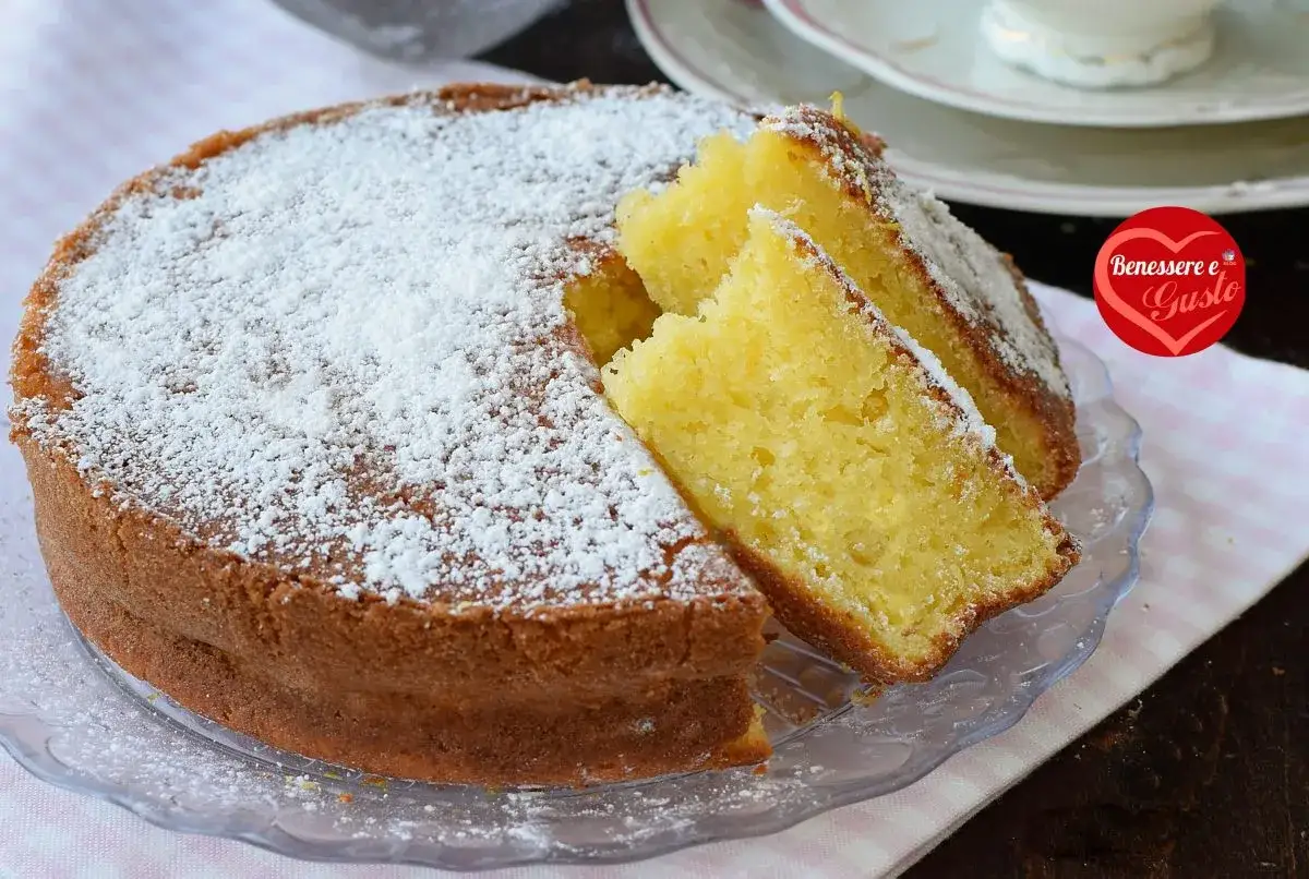 Torta allo yogurt soffice e profumata, cosparsa di zucchero a velo. Due fette sono state tagliate, rivelando l'interno dorato e invitante.