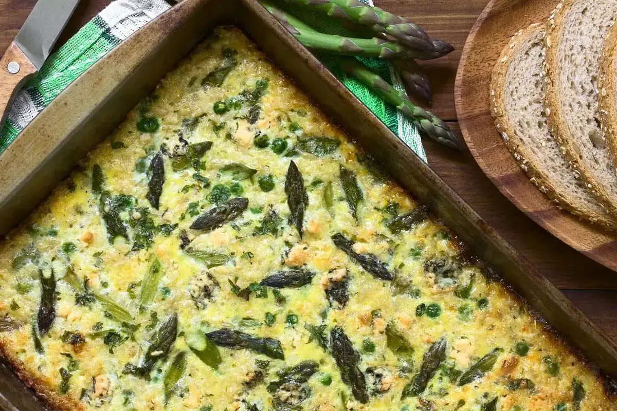 Frittata di asparagi appena sfornata, ricca di verdure fresche e formaggio, pronta per essere gustata con pane integrale.