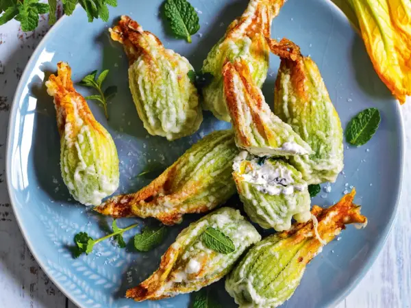 Fiori di zucca fritti, ripieni di formaggio cremoso e guarniti con menta fresca su un piatto blu.