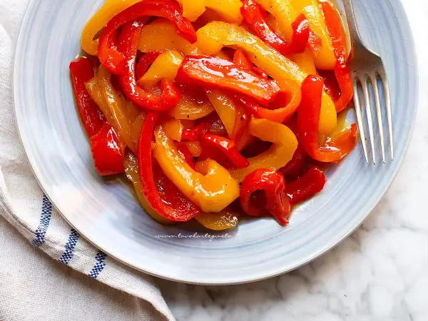 Piatto di peperoni in agrodolce, rossi e gialli, conditi con olio e spezie, pronti per essere gustati.